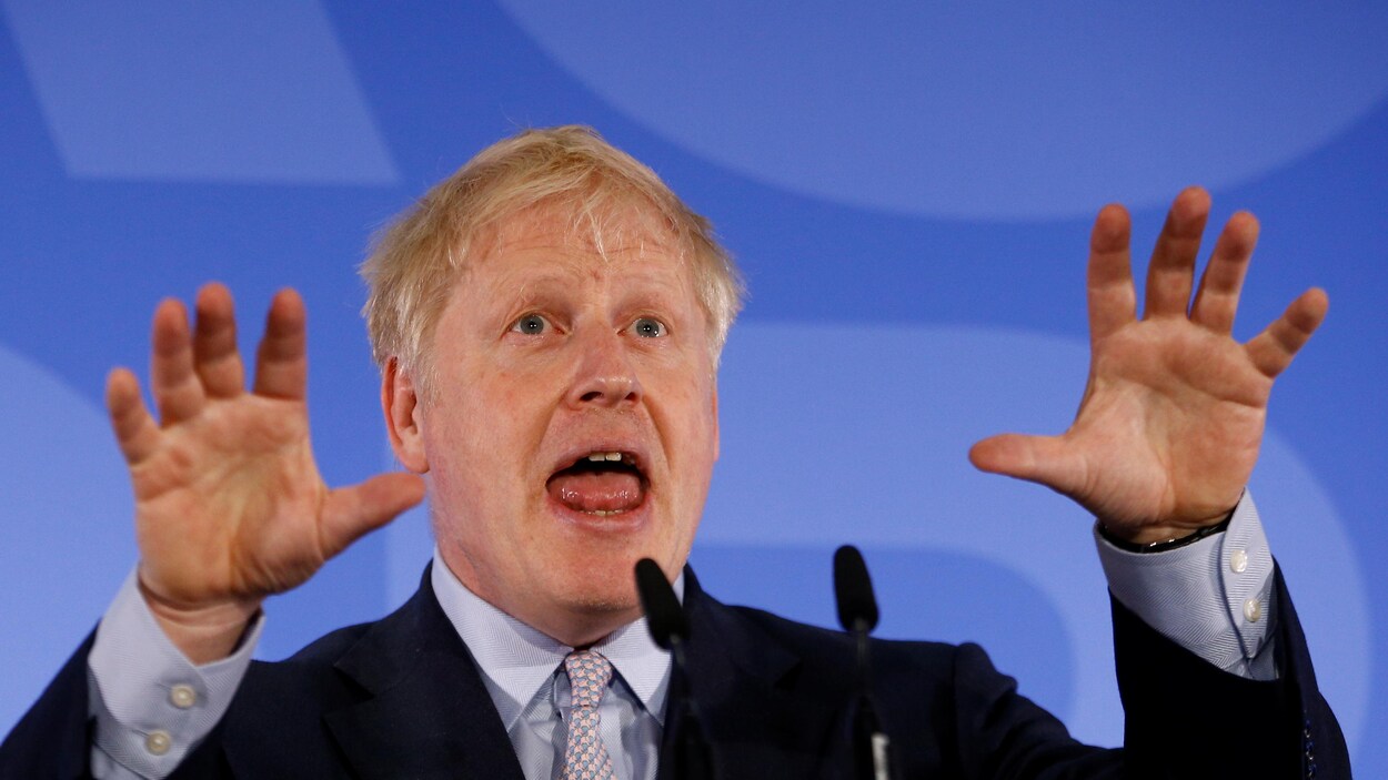 Boris Johnson parle devant des micros, les deux mains en l'air.
