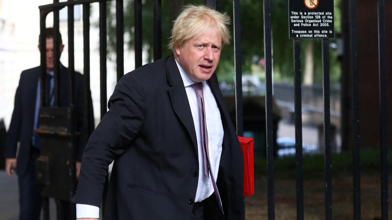 Boris Johnson marche avec un cartable à la main.