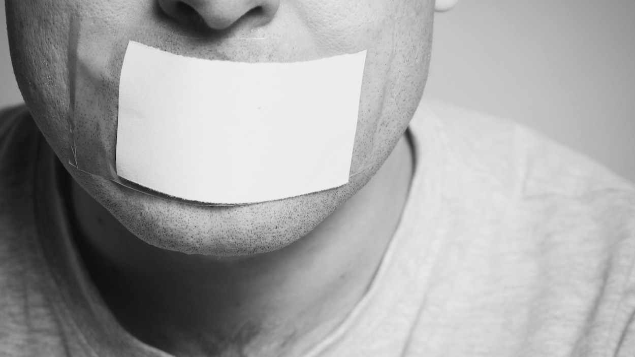 Un homme dont la bouche est masquée par un bout de papier collé à la peau.