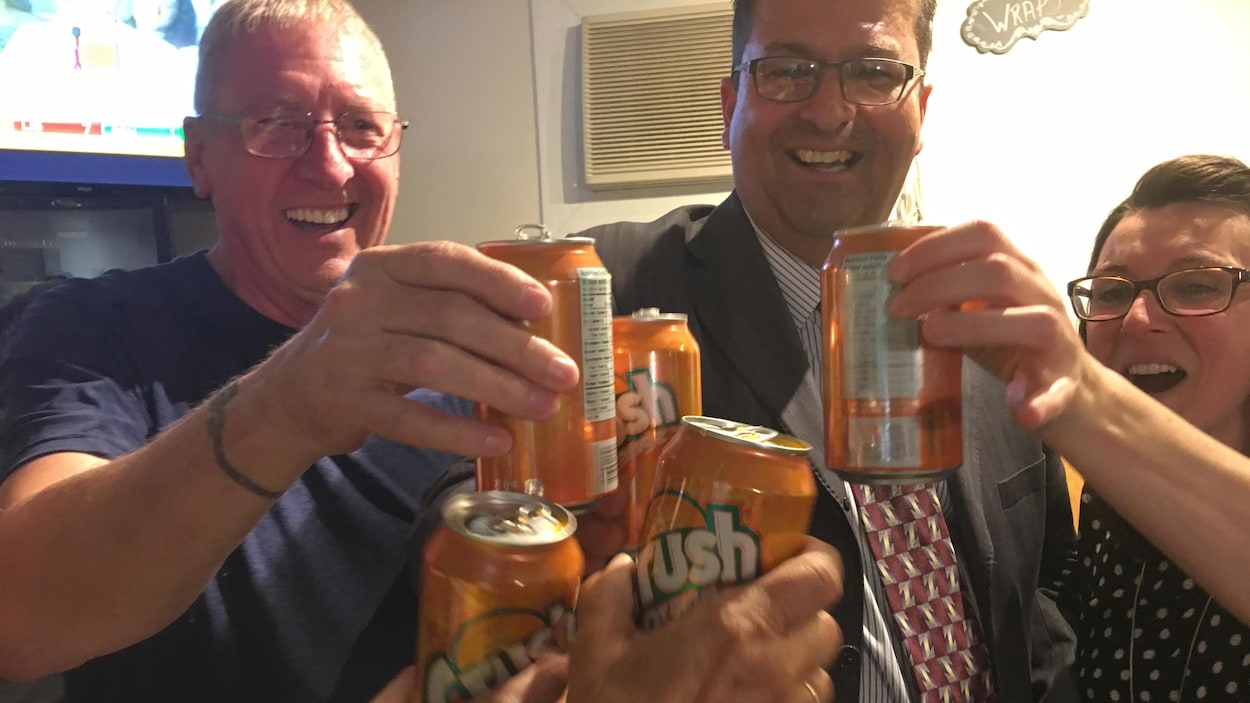 Trois personnes trinquent avec des canettes d'orangeade.