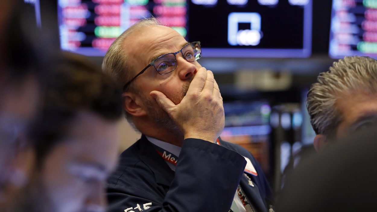 Un courtier à la Bourse de New York regarde les tableaux avec la main droite sur sa bouche.