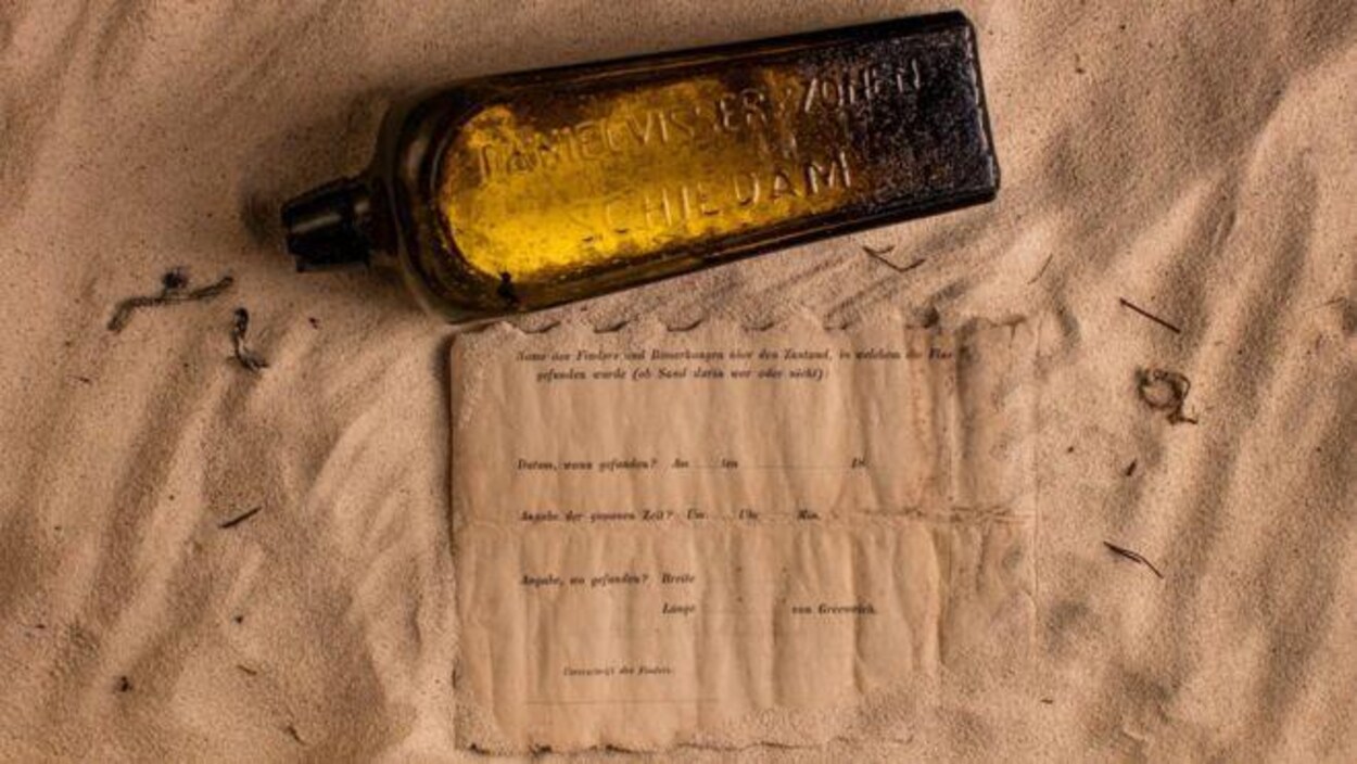 Une bouteille brune et une lettre étendues sur du sable. Une bouteille brune et une lettre étendues sur du sable.