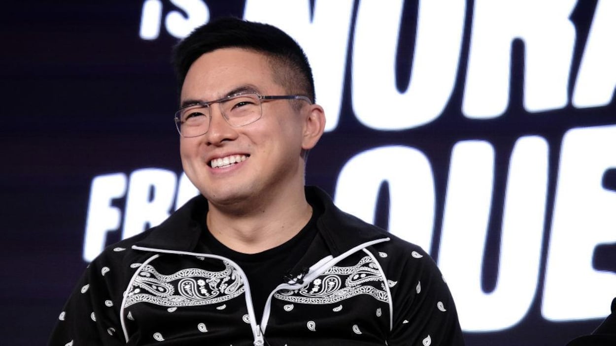 Bowen Yang, qui porte des lunettes, sourit.