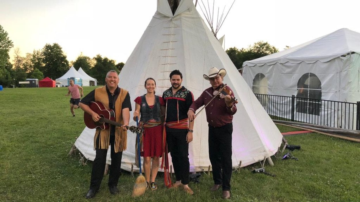 Un guitariste et un violoniste, accompagnés de deux danseurs, sourient à la caméra.