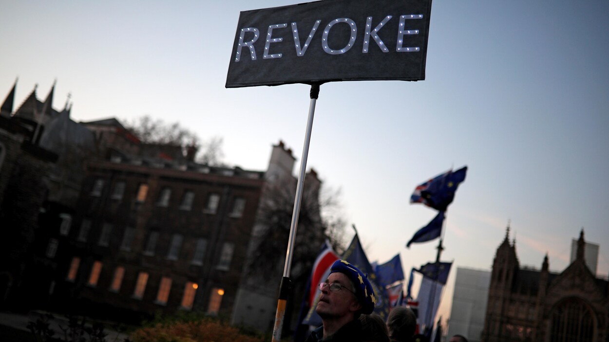 Un homme tient une pancarte sur laquelle est écrit : « revoke ».
