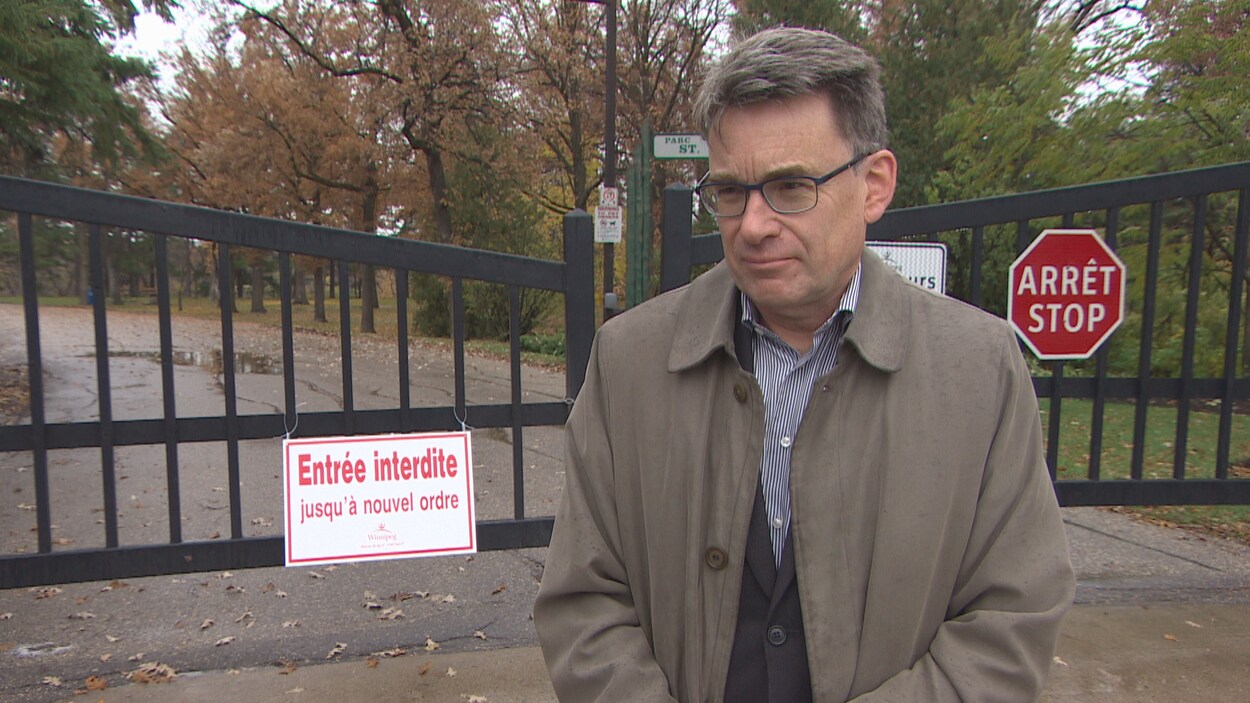 Un homme se tient devant la clôture d'un parc sur laquelle un panneau indique : Entrée interdite jusqu'à nouvel ordre.