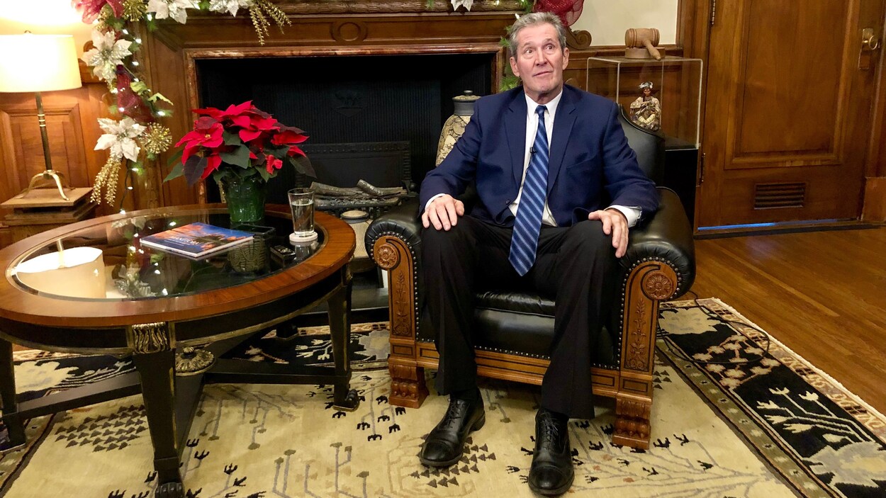 Brian Pallister est assis dans un fauteuil de cuir près d'une table basse et d'un foyer décoré pour Noël.