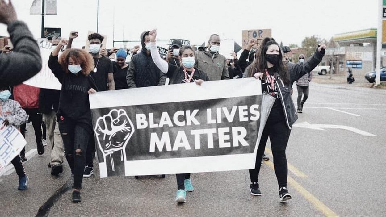 Des manifestants tiennent une banderole sur laquelle est inscrite Black Lives Matter avec leurs poings en l'air.