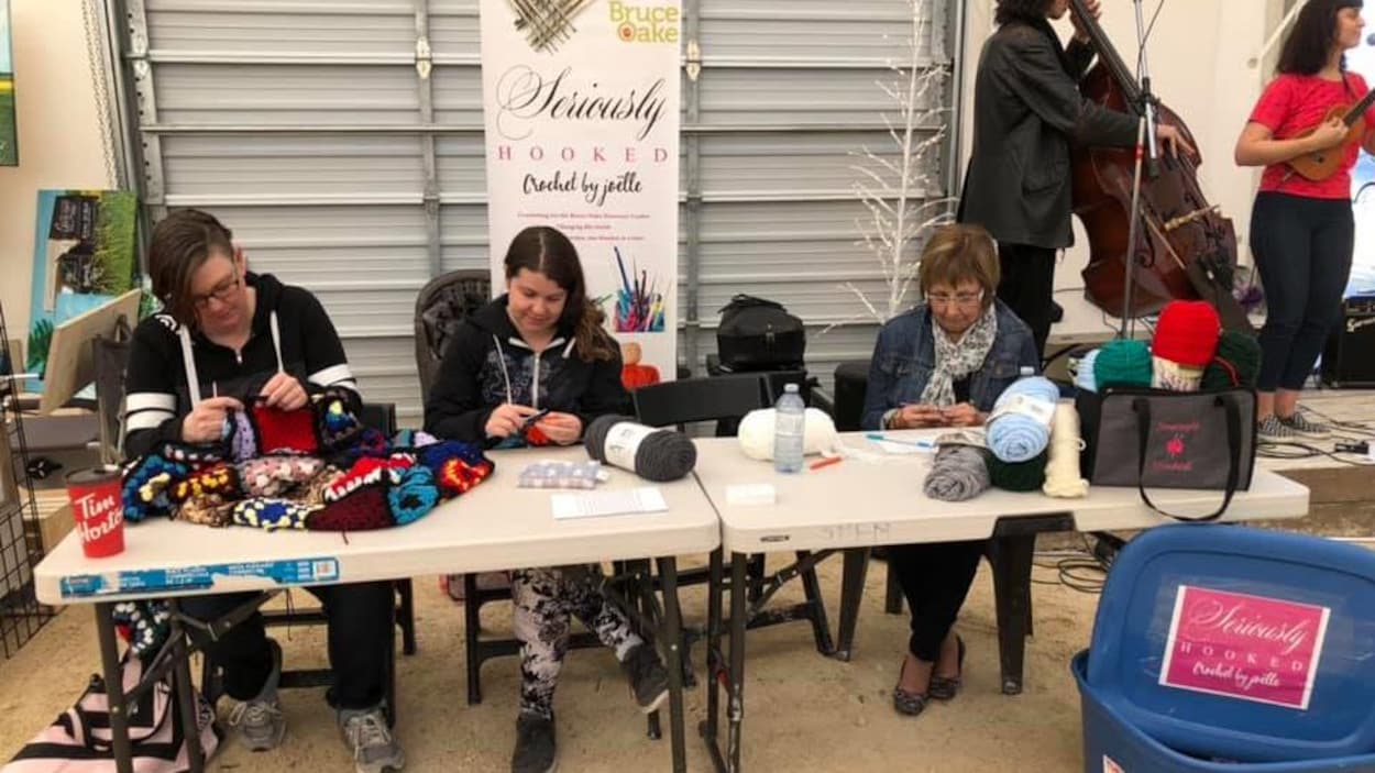 Trois femmes sont installées à une table dans un marché et crochètent.