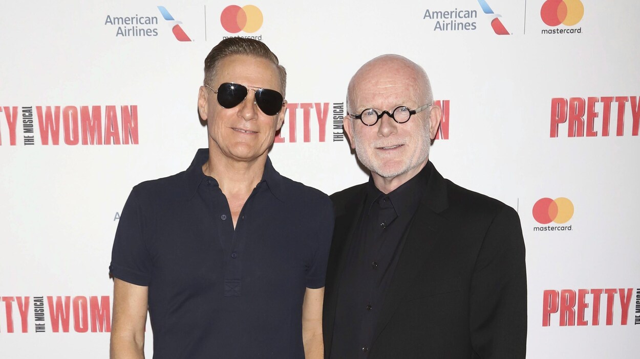 Les deux hommes se tiennent sur le tapis rouge et sourient.