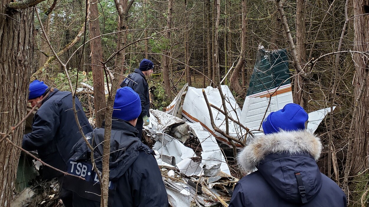 Des enquêteurs sont sur le lieu d'un écrasement d'avion dans une zone boisée avec les débris d'un avion.