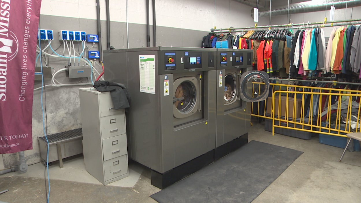 Deux laveuses commerciales à côté desquelles des vêtements sont suspendus à des cintres.