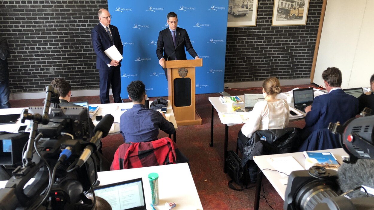 Brian Bowman debout derrière un lutrin, adresse la parole aux journalistes assis devant lui dans une salle de l'hôtel de ville.