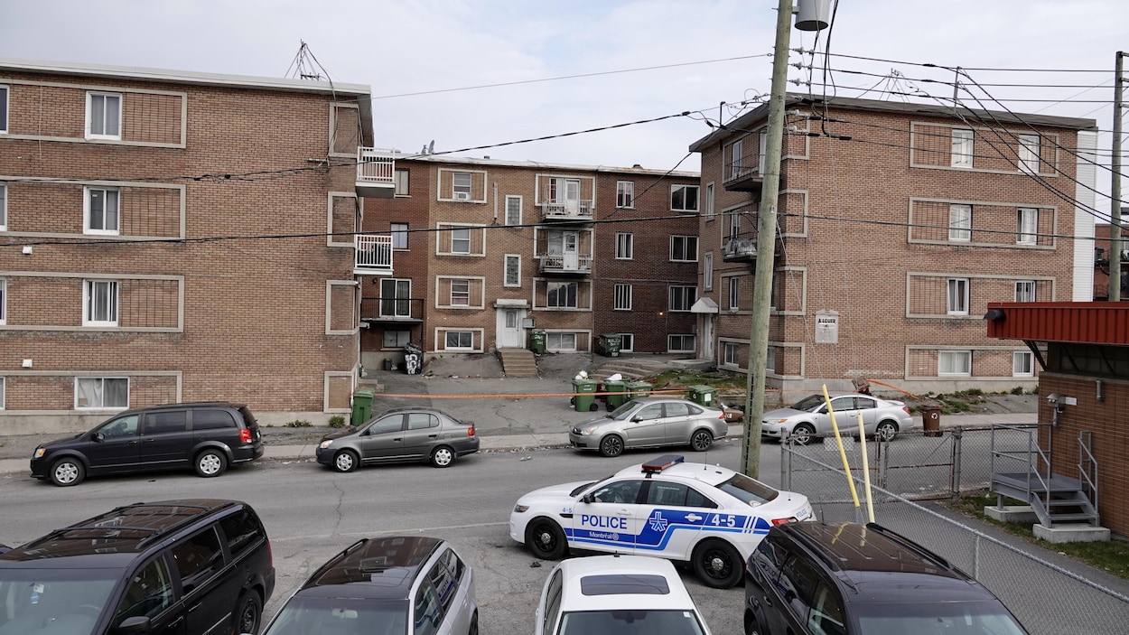 Une voiture de police est stationnée devant des immeubles d'appartements, où un cordon de sécurité a été installé.