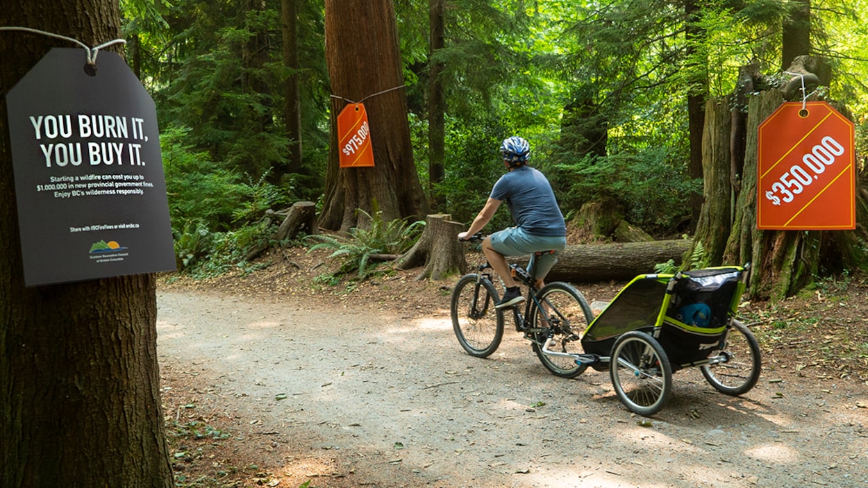 Un cycliste sur un sentier où sont attachées des étiquettes de prix géantes de 350 000 $ et de 975 000 $