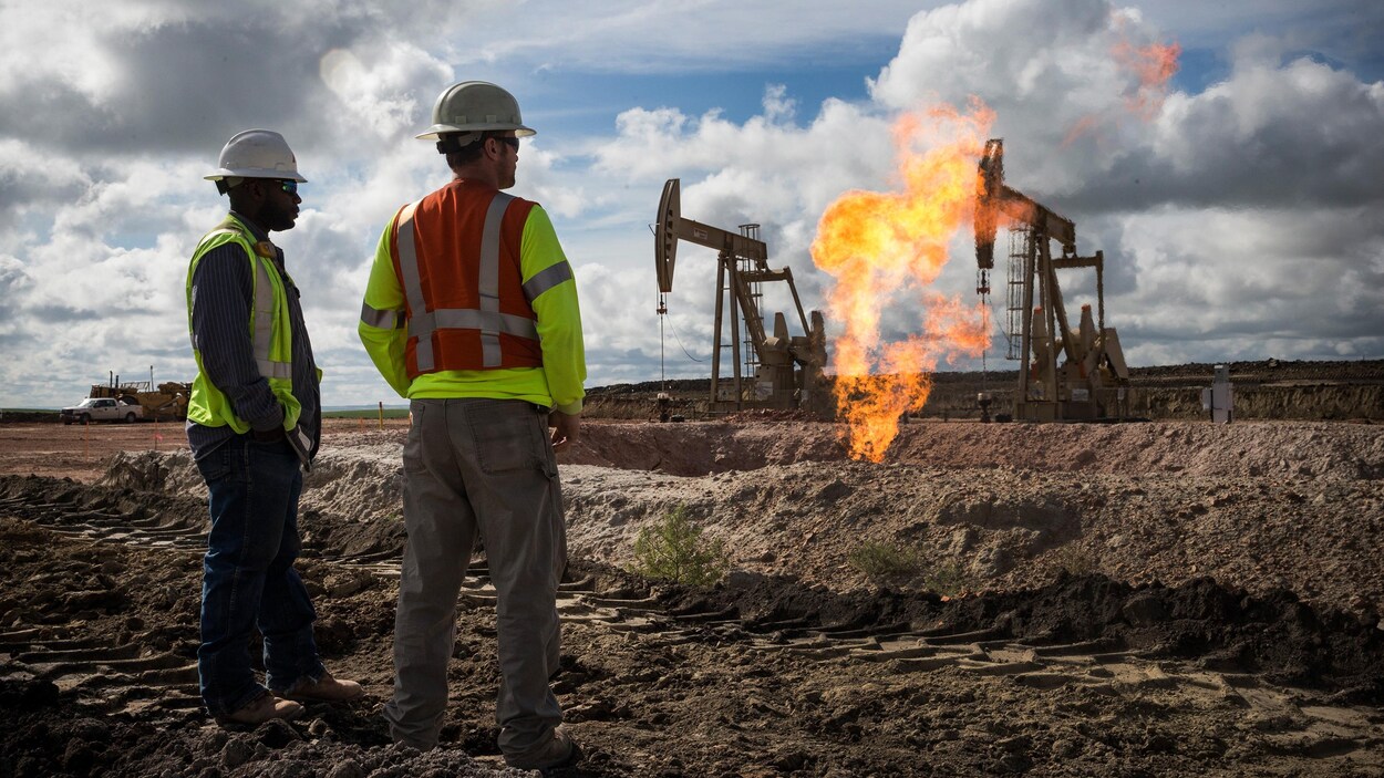 Deux travailleurs regardent des puits de pétrole.