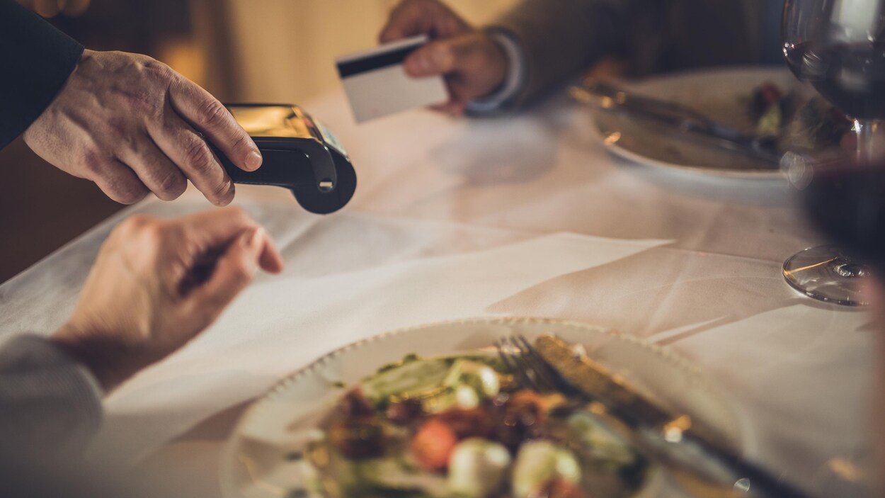 Une main avec une carte de crédit, une autre avec une machine interac, des assiette. Personne n'est reconnaissable. Une main avec une carte de crédit, une autre avec une machine interac, des assiette. Personne n'est reconnaissable.