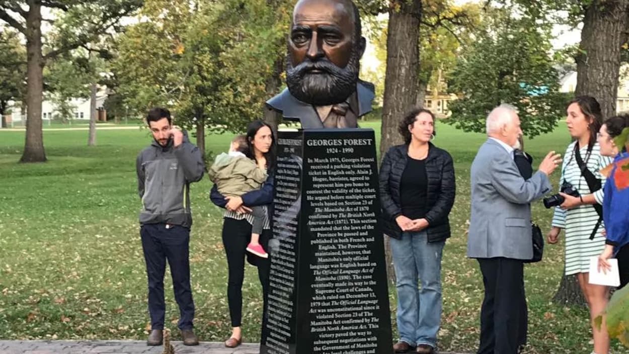 Des gens réunis autour d'un buste en bronze.