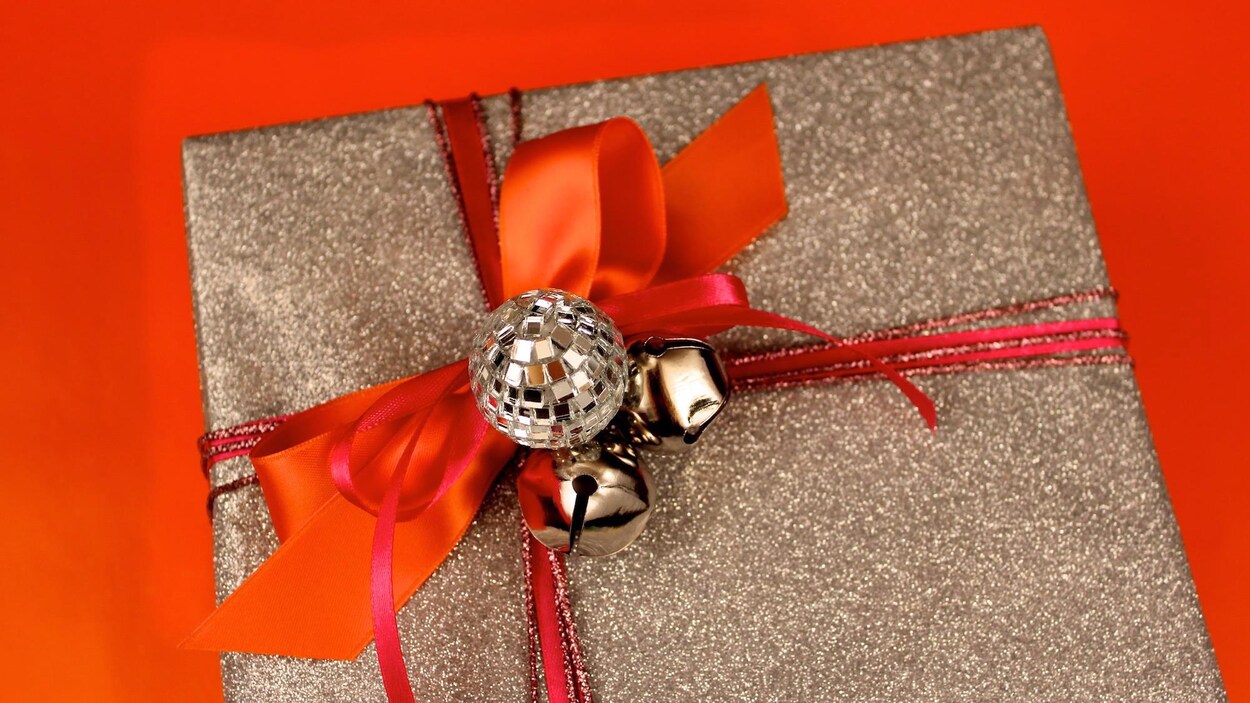 Photo d'un cadeau de Noël enveloppé de papier brun et entouré de ruban et d'une boucle rouges.