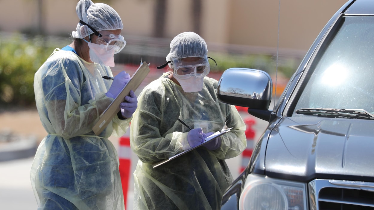 Deux personnes en habit de protection prennent des notes près d'une voiture.