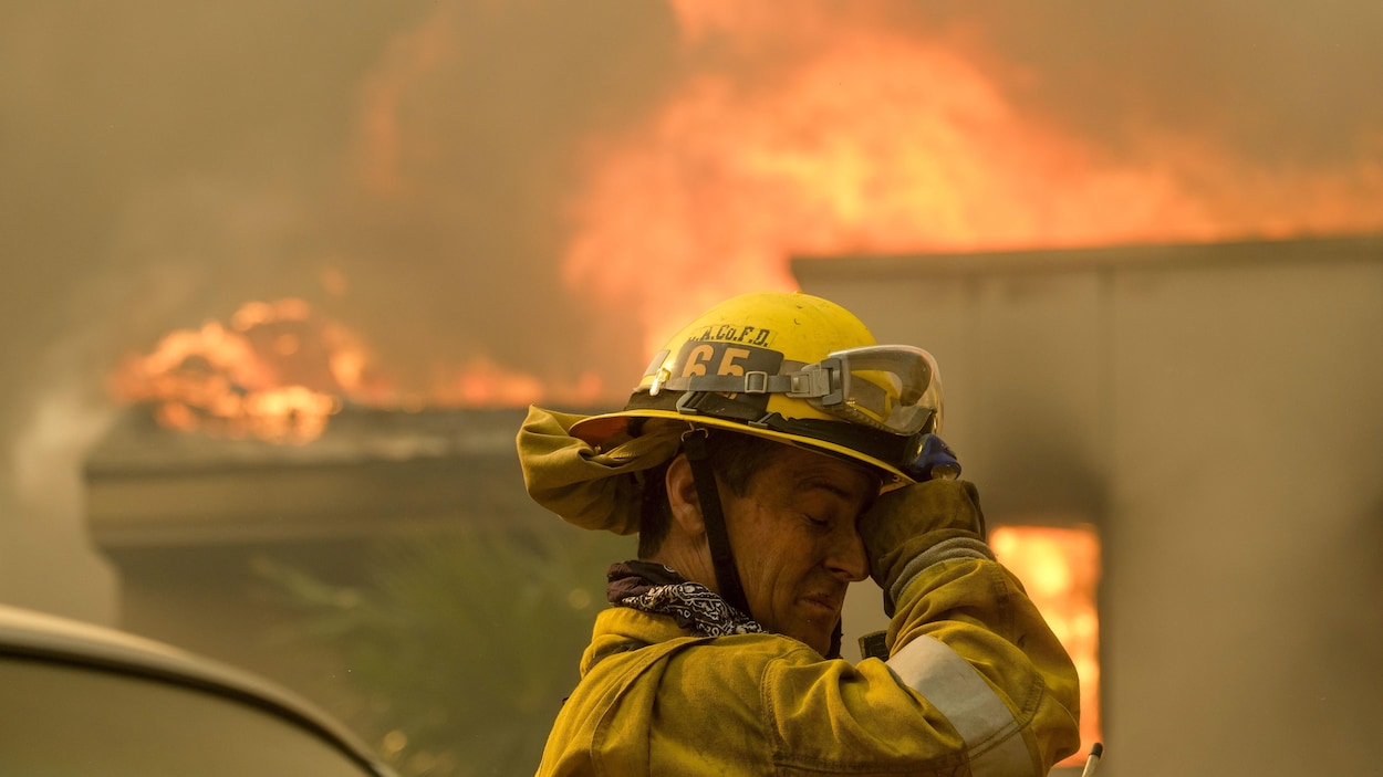 Un pompier se frotte les yeux devant une maison en flammes.