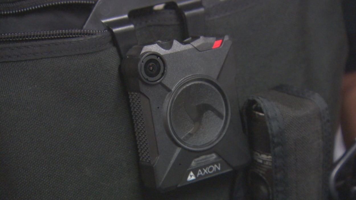 Zoom sur la caméra, plus petite qu'un téléphone cellulaire, sur le gilet d'un policier.