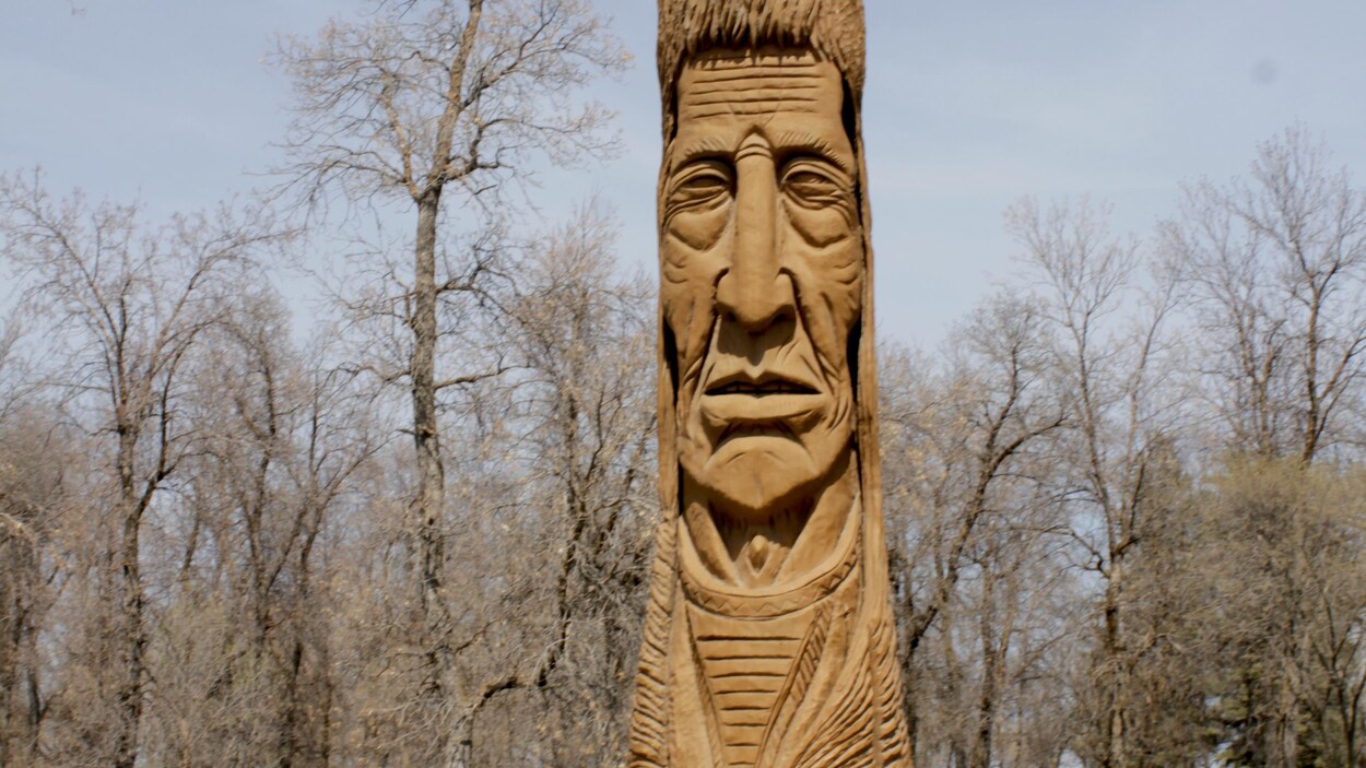 Cameron Adams a côté d'une grande statue de bois à l'effigie d'un chef autochtone.
