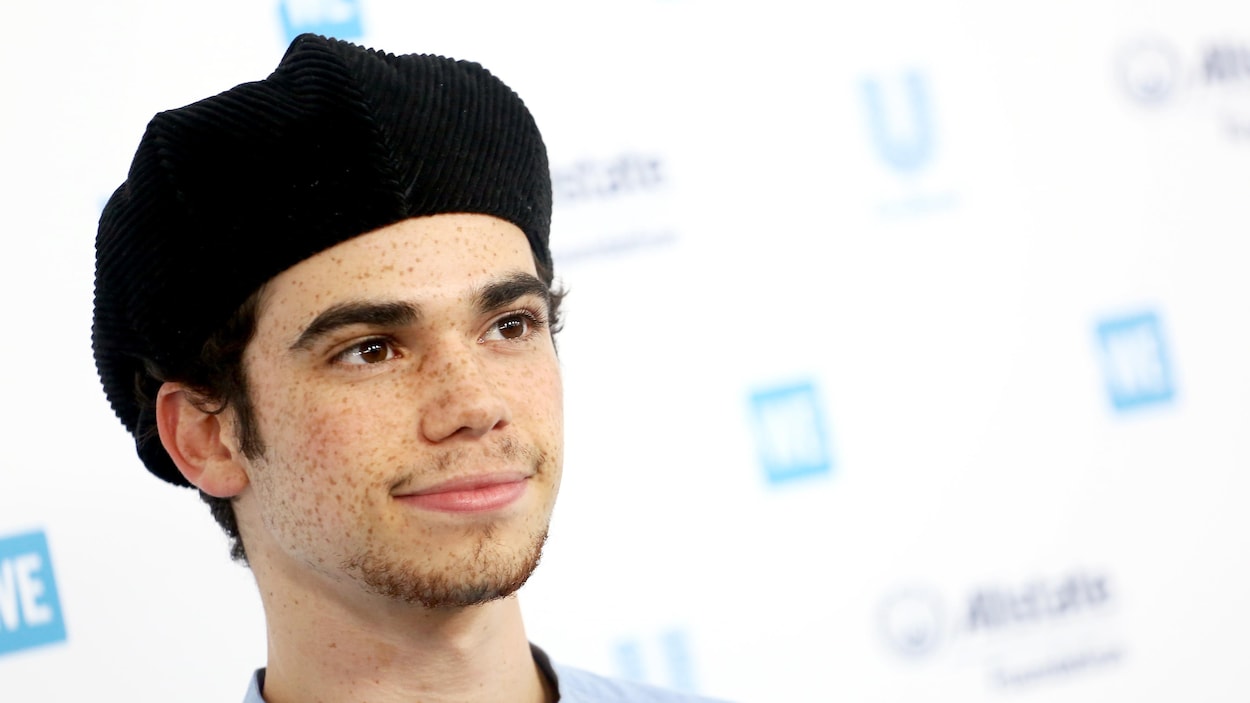 Cameron Boyce porte un béret noir et sourit légèrement en regardant droit devant lui.