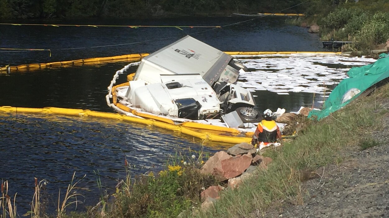 Un camion tombé dans un lac entouré de bouées antipollution. Un camion tombé dans un lac entouré de bouées antipollution.