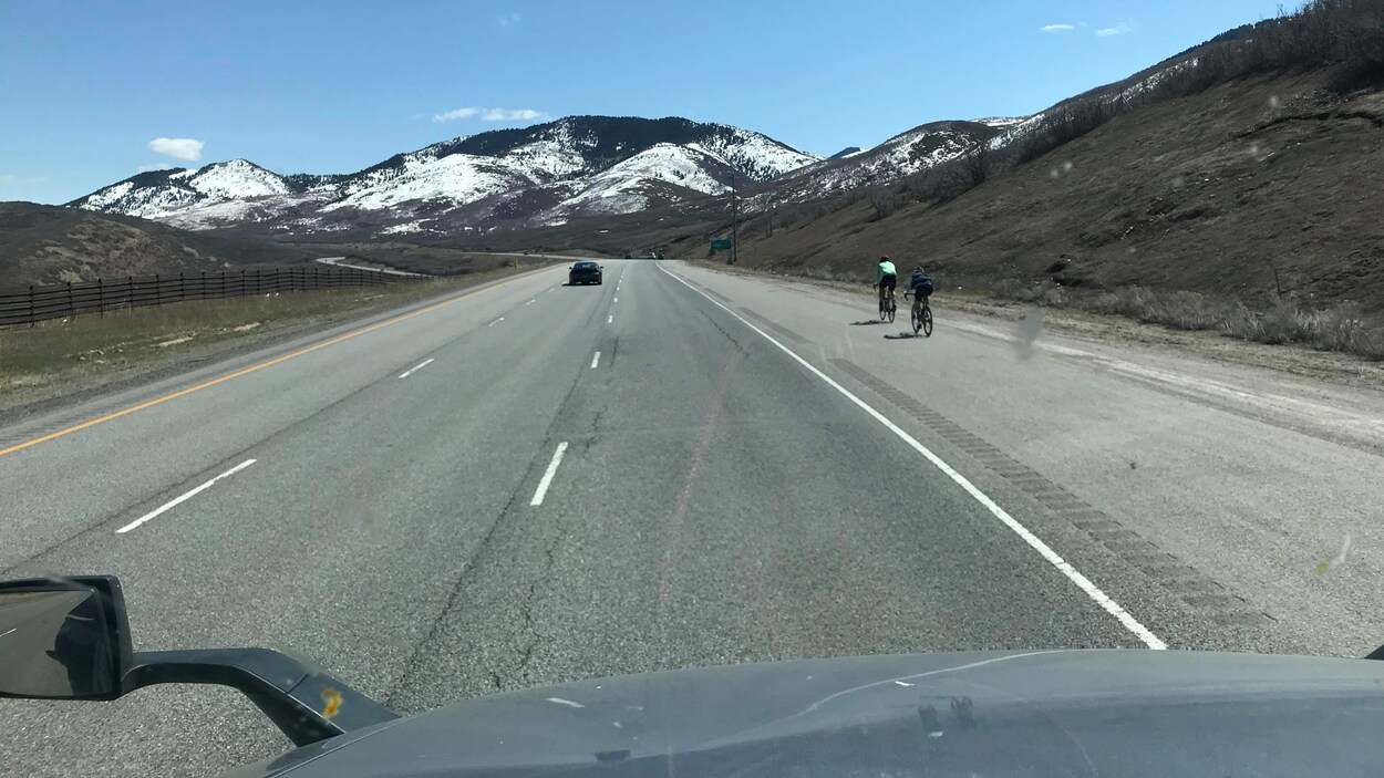 Une route presque déserte et des montagnes enneigées au loin.