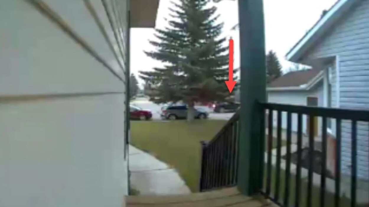 Image un peu floue d'une caméra de surveillance installée sur une maison et qui pointe vers la rue où un véhicule noir se trouve. Une flèche rouge qui pointe vers le véhicule en question a été dessinée.