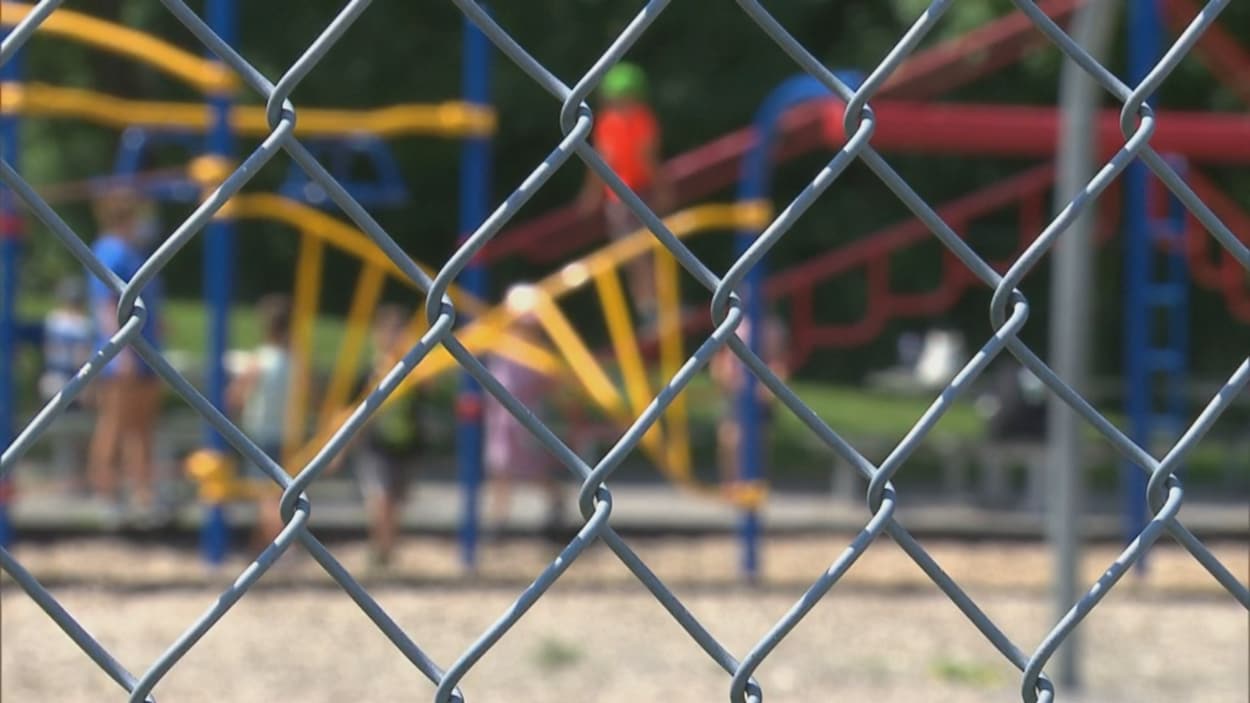 Des enfants jouent dans un module de jeux, derrière une clôture.