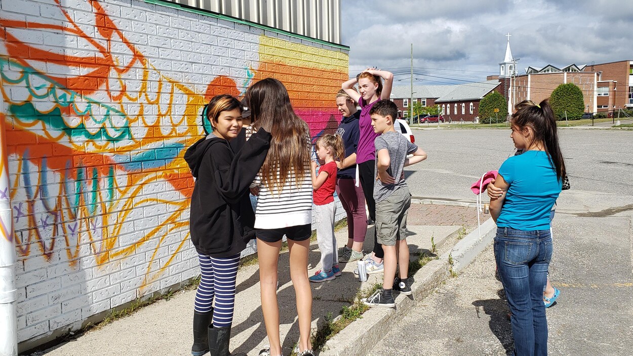 Des jeunes peignent une murale sur un édifice.