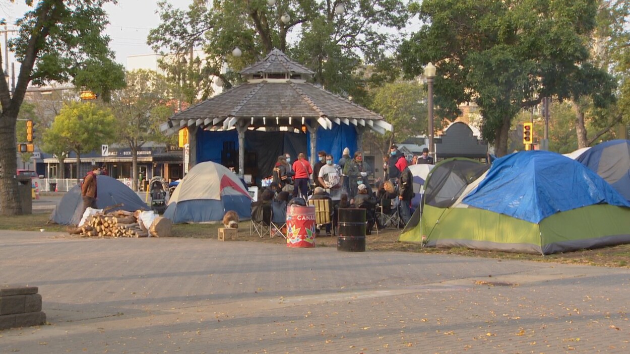 Des tentes autour d'un pavillon dans un petit parc. Des gens se promènent.
