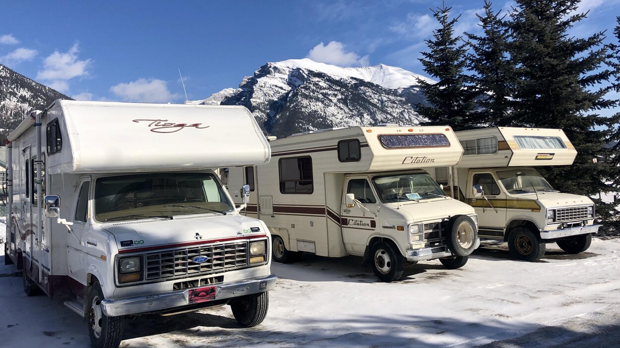 Trois caravanes stationnées les unes à côté des autres. Derrière elles, on voit les Rocheuses. Le ciel est complètement dégagé. C'est l'hiver, on voit de la neige sur le sol.