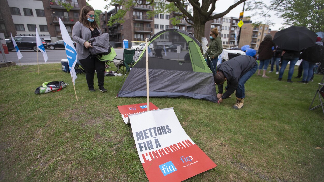 Deux personnes installent une tente devant une pancarte sur laquelle est écrit : «Mettons fin à l'inhumain».