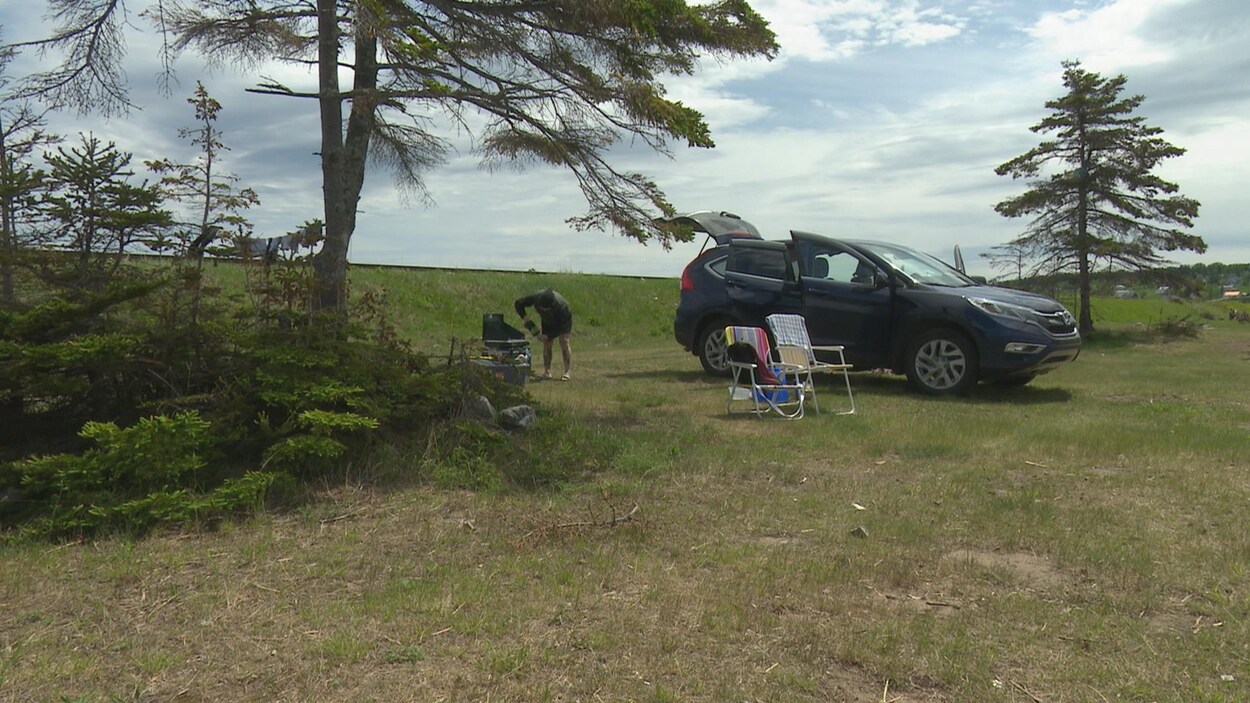 Une campeuse s'installe. On voit sa voiture, des chaises et un poêle barbecue.