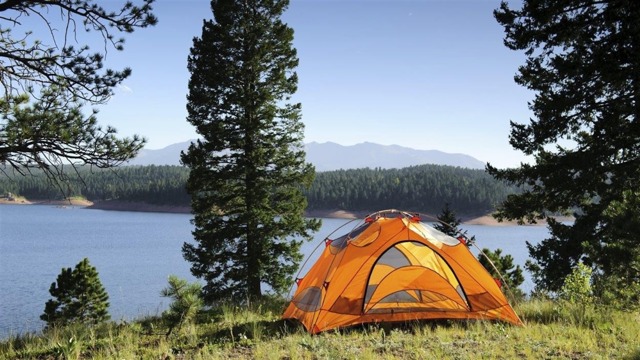 Une tente sur un terrain surplombant un lac.