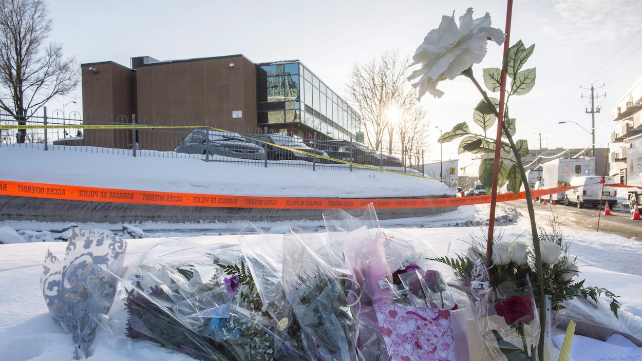 Des fleurs dans la neige devant un grand bâtiment entouré d'un ruban de police jaune.