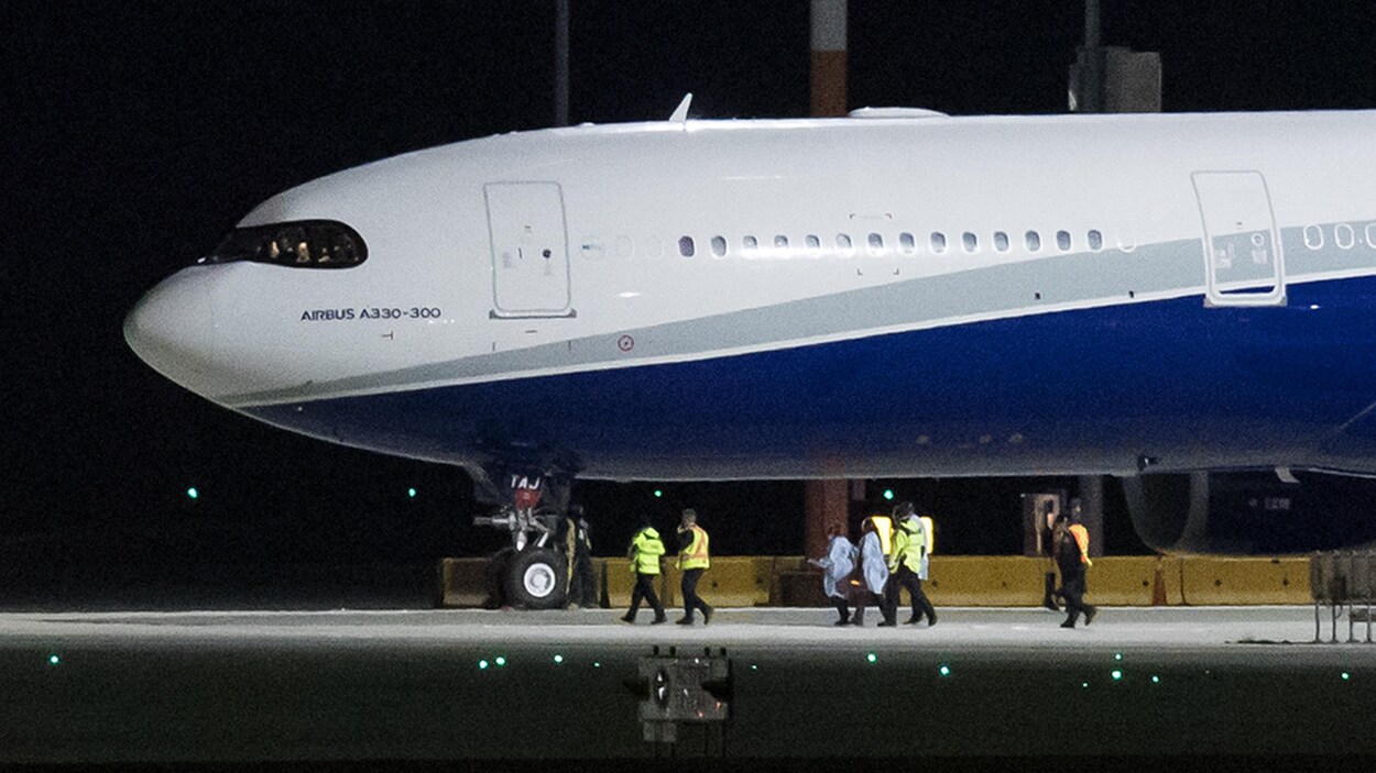 Des officiels marchent vers un appareil qui vient de se poser sur le tarmac.