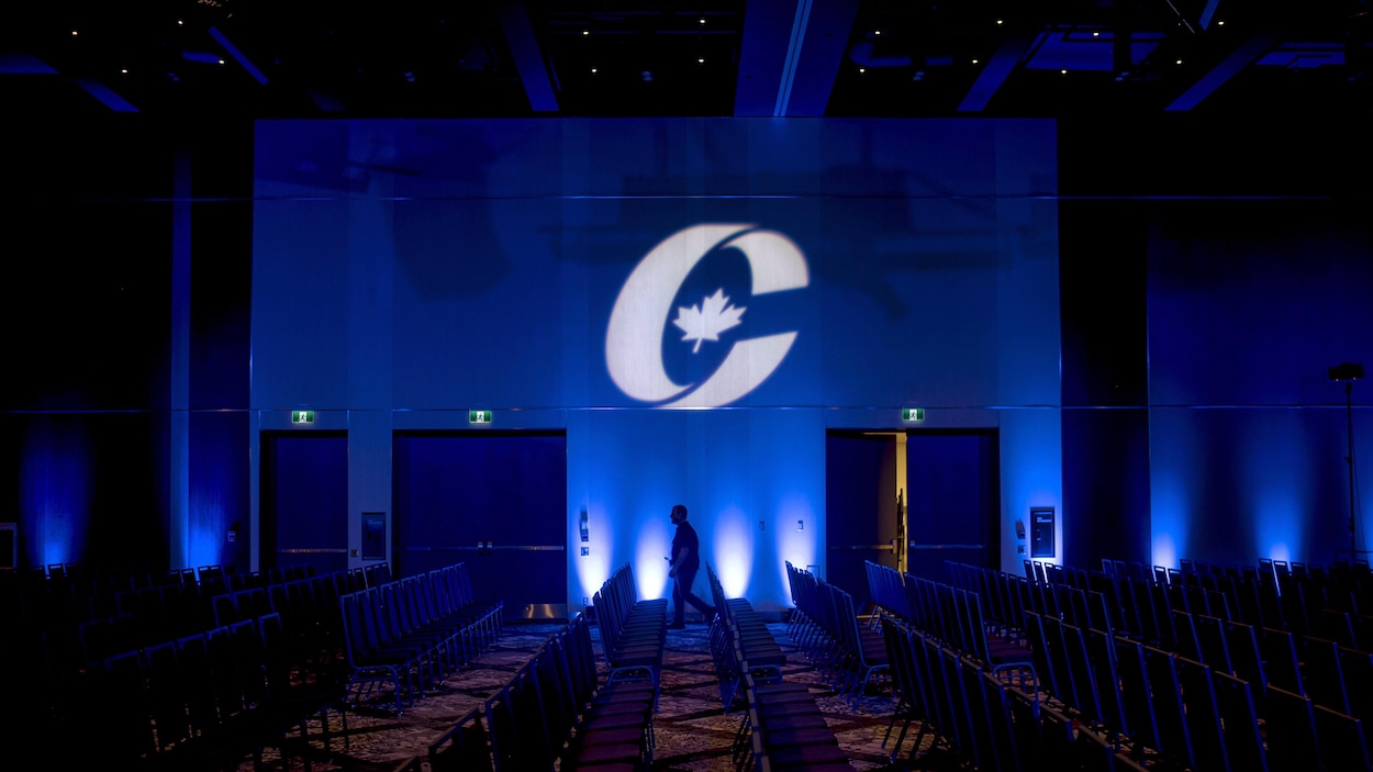 Un homme, de loin, marche devant un drapeau du Parti conservateur du Canada avant l'ouverture du congrès du parti en août 2018 à Halifax.