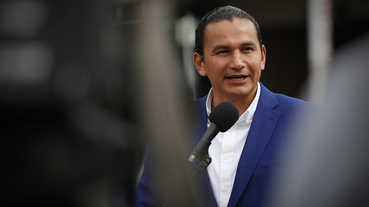 Wab Kinew parle avec les médias le 9 septembre. Il est vêtu d'un veston bleu sur une chemise blanche.