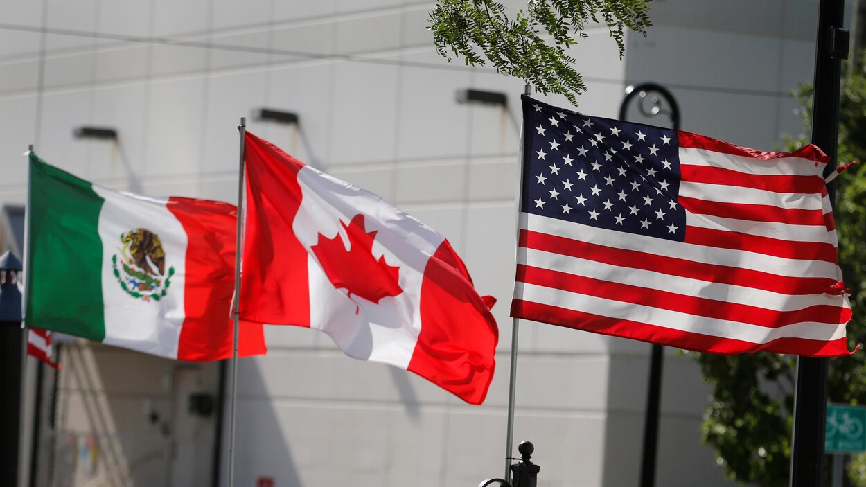 Trois drapeaux différents flottent près d'un bâtiment lors d'une journée ensoleillée.