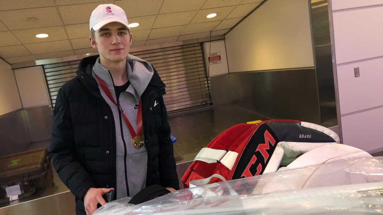 Joel Hofer à l'aéroport avec son équipement de gardien sur un chariot et une médaille d'or autour du cou.