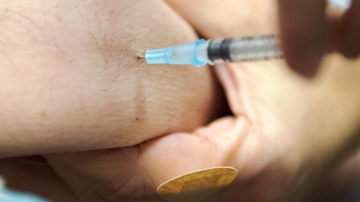 Gros plan sur une seringue dont l'aiguille s'enfonce dans la peau d'un patient.