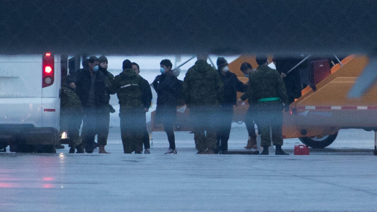 Des passagers masqués sont accueillis par des militaires sur le tarmac d'un aéroport.