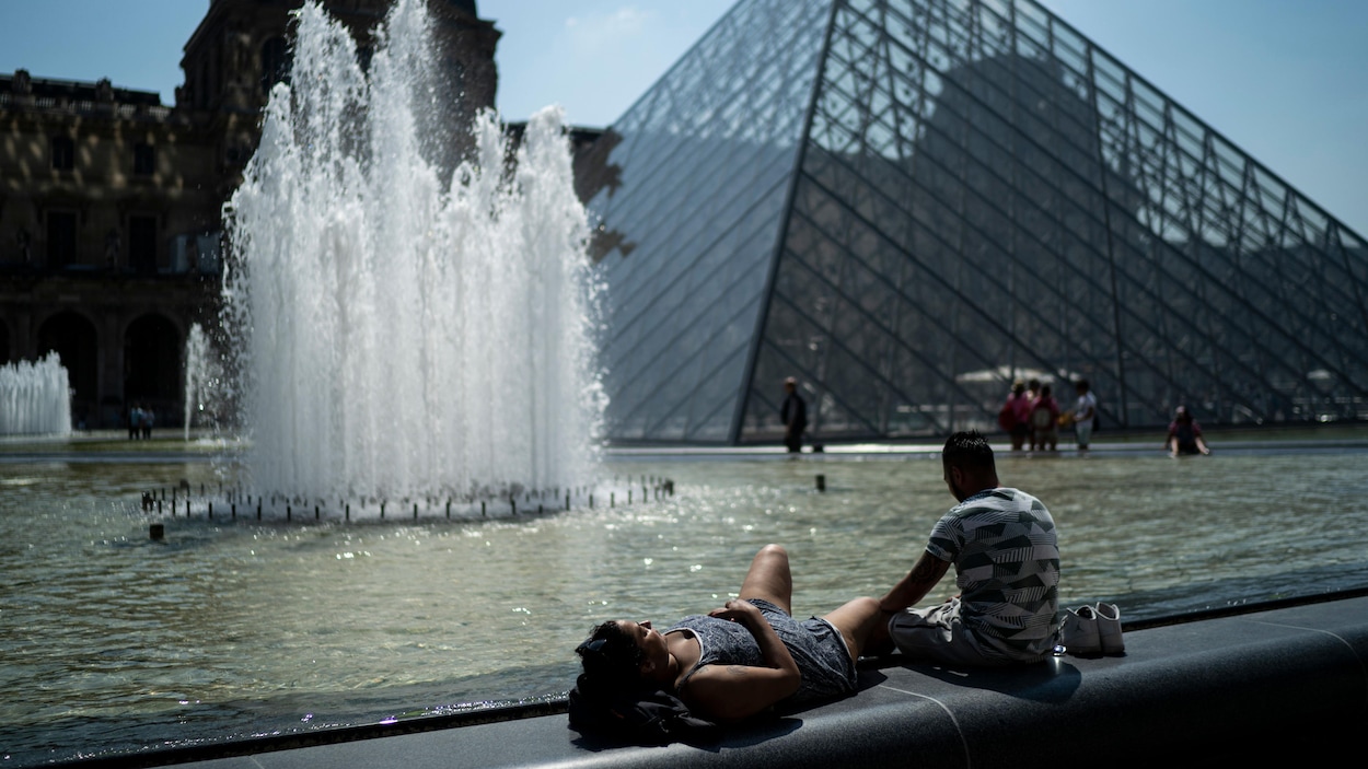 Une femme est étendue et prend un bain de soleil en compagnie d’un homme aux abords de la Pyramide du Louvre, à Paris.