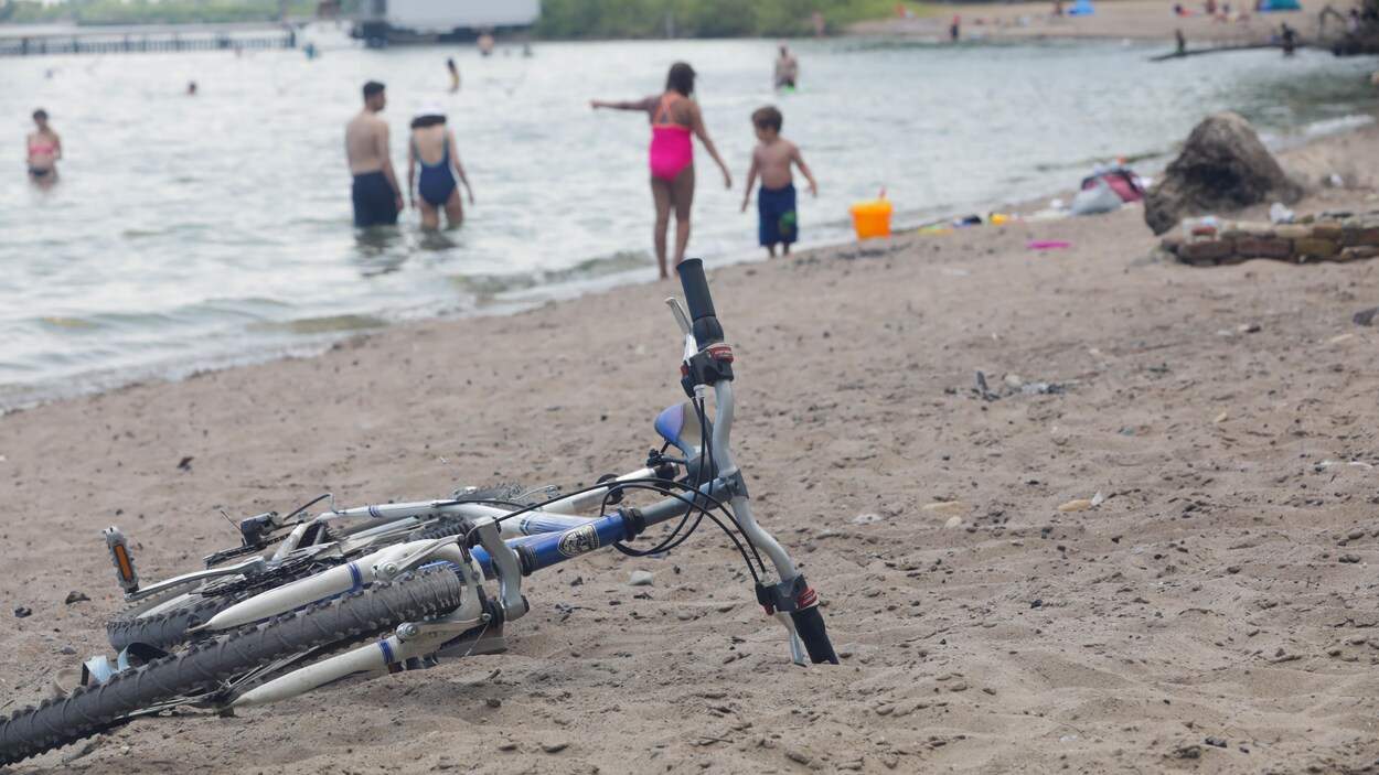 Une bicyclette dans le sable et des personnes qui se baignent à la plage.