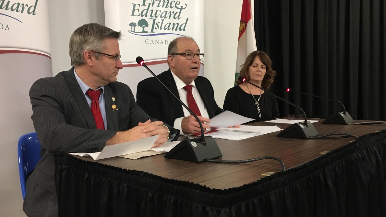 Le ministre Allen Roach entouré de deux autres intervenants
