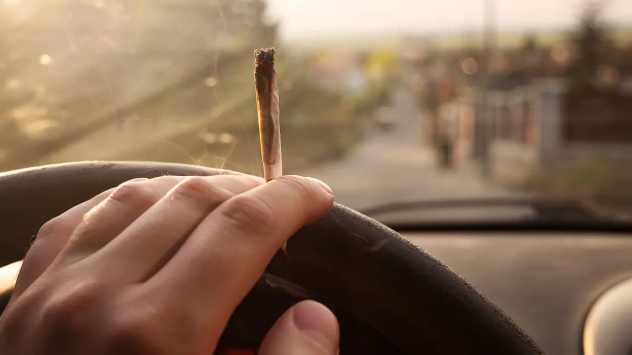 Une main tient un joint de cannabis et tient le volant d'une voiture.